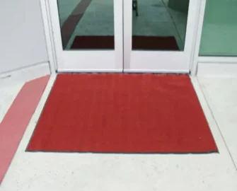 Red Soft Top Olefin Door Mat displayed in front of a door entrance.