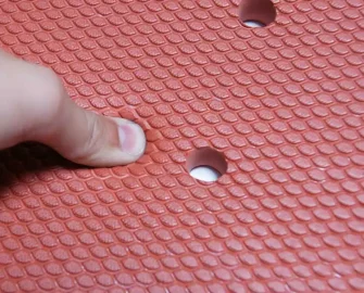 someone pressing down with their finger on a red mat with holes along the inside