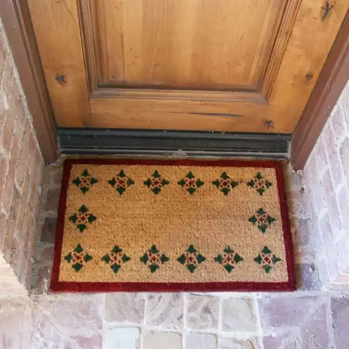 Brown mat with 4 green triangles made in a repeating pattern along its perimeter in front of a door entrance.