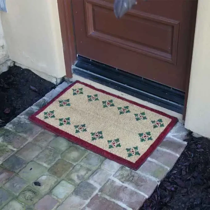 Brown mat with 4 triangles pattern along its perimeter in front of a dimly lit porch.