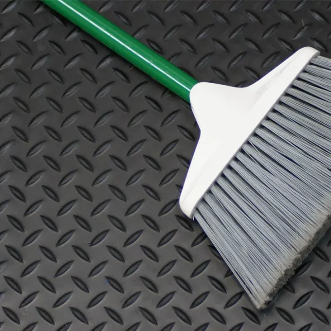 Green handled broom on top of a black diamond plate mat