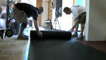 Two men helping each other roll out rubber mats