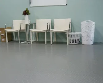 Coin grip metallic flooring underneath 3 chairs, a laundry basket, a laundry bin, and a bag with a whiteboard in the background