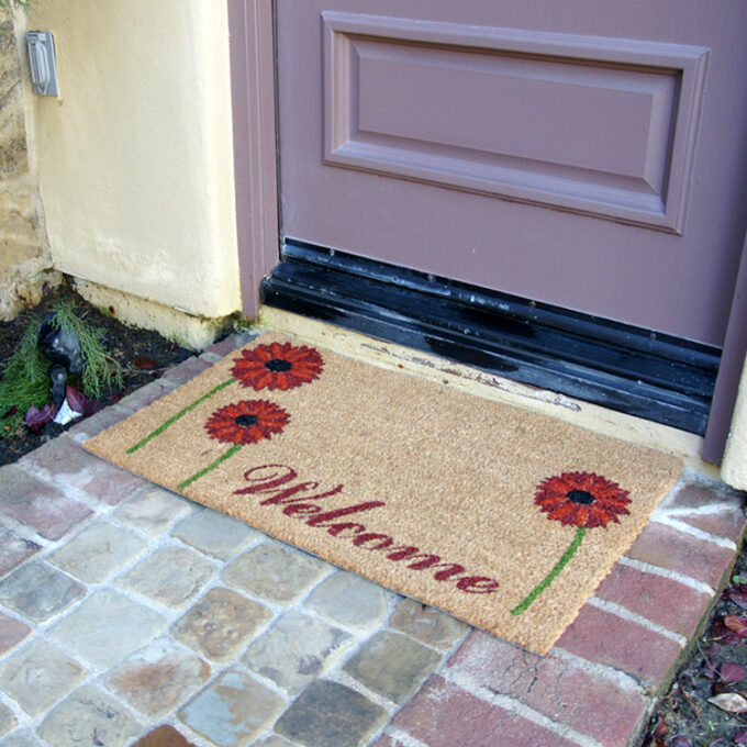 Far shot angled of red daisies doormat in front of door entrance